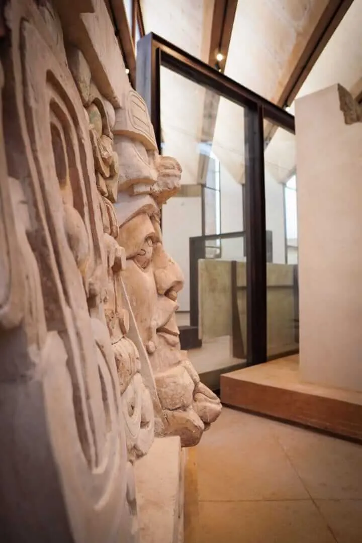 The Museo Regional de la Costa Oriental: A Cultural Turning Point for Tulum Carved stone relief sculptures depicting human faces are displayed on a museum wall with glass partitions and wooden flooring visible in the background