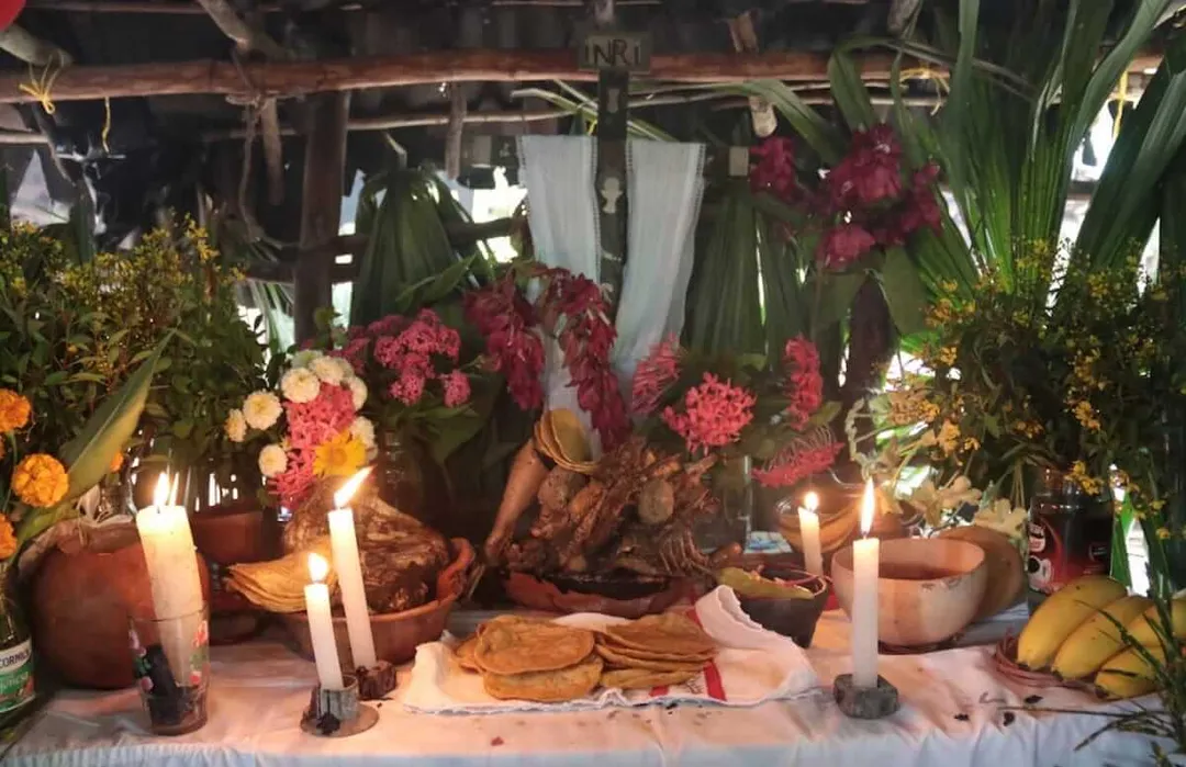 An altar decorated with hanging flowers, candles, clay vessels, and food items under a wooden structure with draped fabric