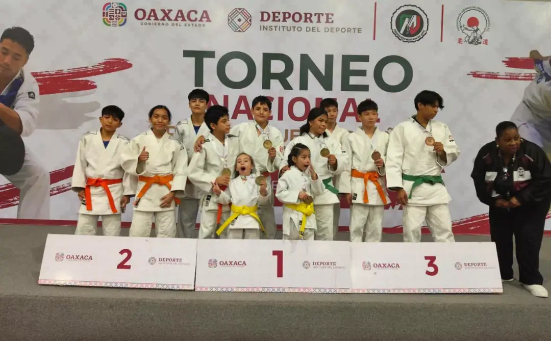 Young judo competitors in white uniforms and colored belts stand on a podium with officials at a national tournament