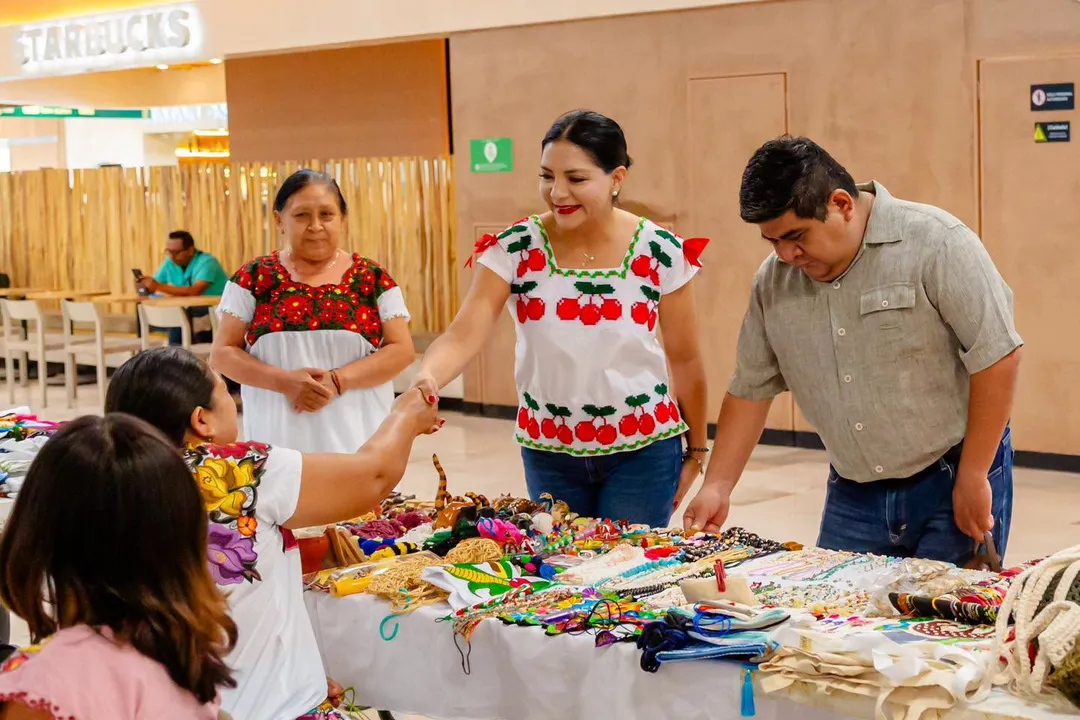 Local artisans land a permanent sales point inside the new Tulum airport Group of people gathered around a table displaying colorful handmade crafts and textiles in an airport terminal