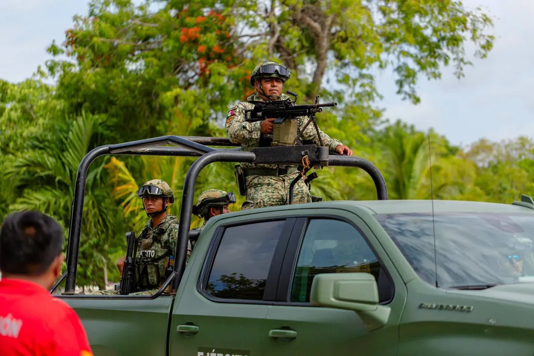 Hotel Zone and Downtown Get Permanent Patrols Through Peak Tourist Weeks Armed personnel in camouflage uniforms stand in the bed and cab of a military-style pickup truck during a patrol in a tropical setting with palm trees and fruit