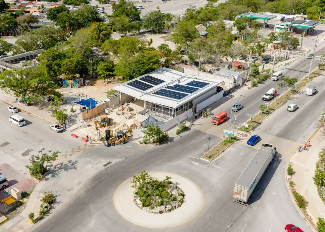 Aerial view of a commercial building with solar panels on its roof surrounded by parking areas, roads, and construction equipment in a tropical setting