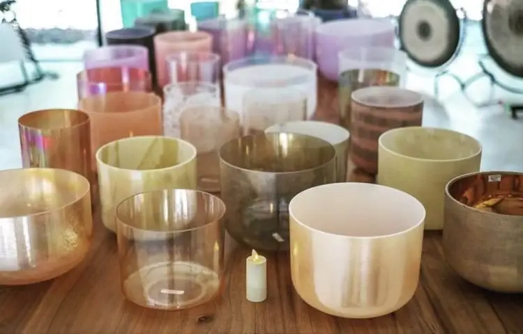 Singing bowls and sound healing instruments arranged on a wooden table with a small candle between them Singing bowls and sound healing instruments arranged on a wooden table with a small candle between them