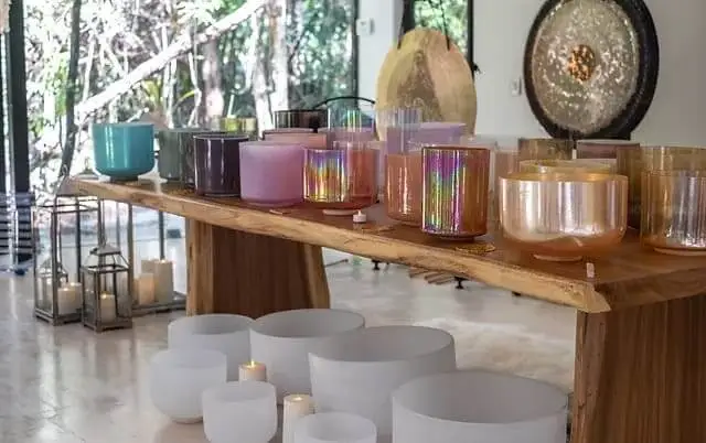 Various candles and singing bowls arranged on a wooden shelf and floor in a bright room with windows overlooking greenery Various candles and singing bowls arranged on a wooden shelf and floor in a bright room with windows overlooking greenery