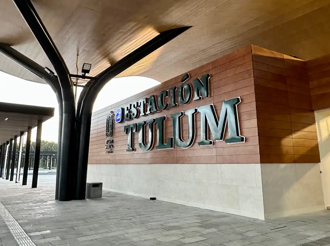 A transit station entrance with "Estación Tolum" signage mounted on a brick and concrete wall beneath a modern covered canopy structure