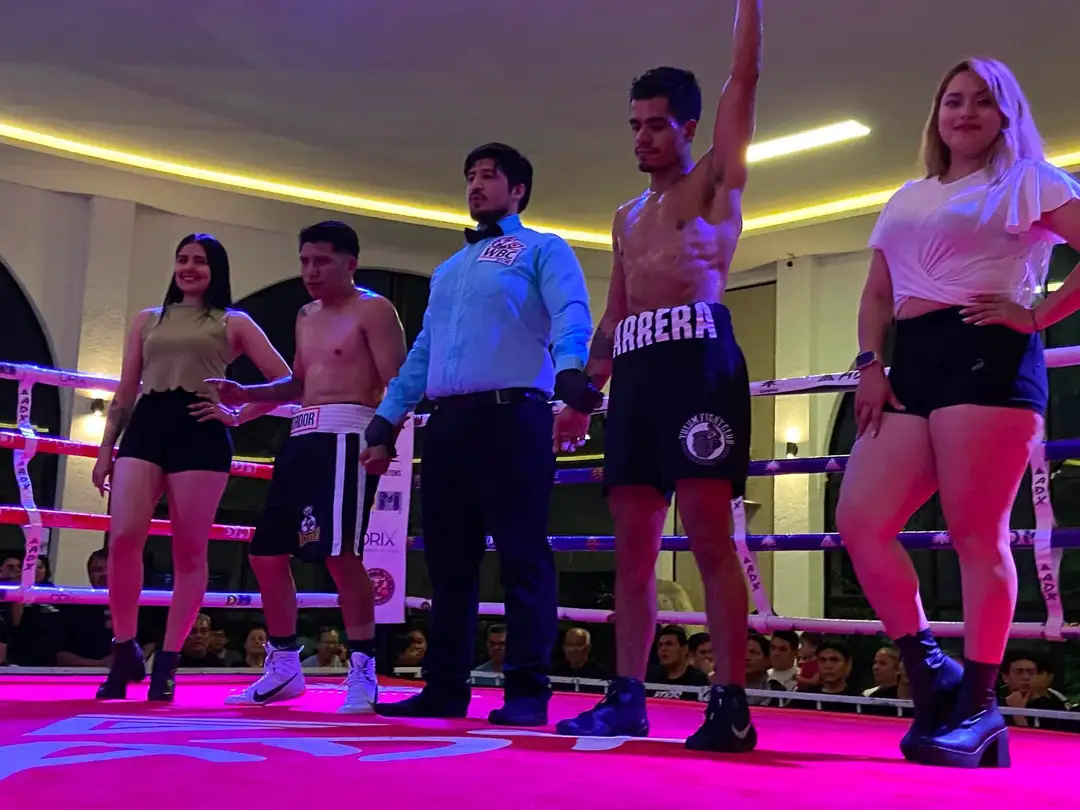 Wrestlers and officials stand in a boxing ring with neon pink and blue lighting during an event