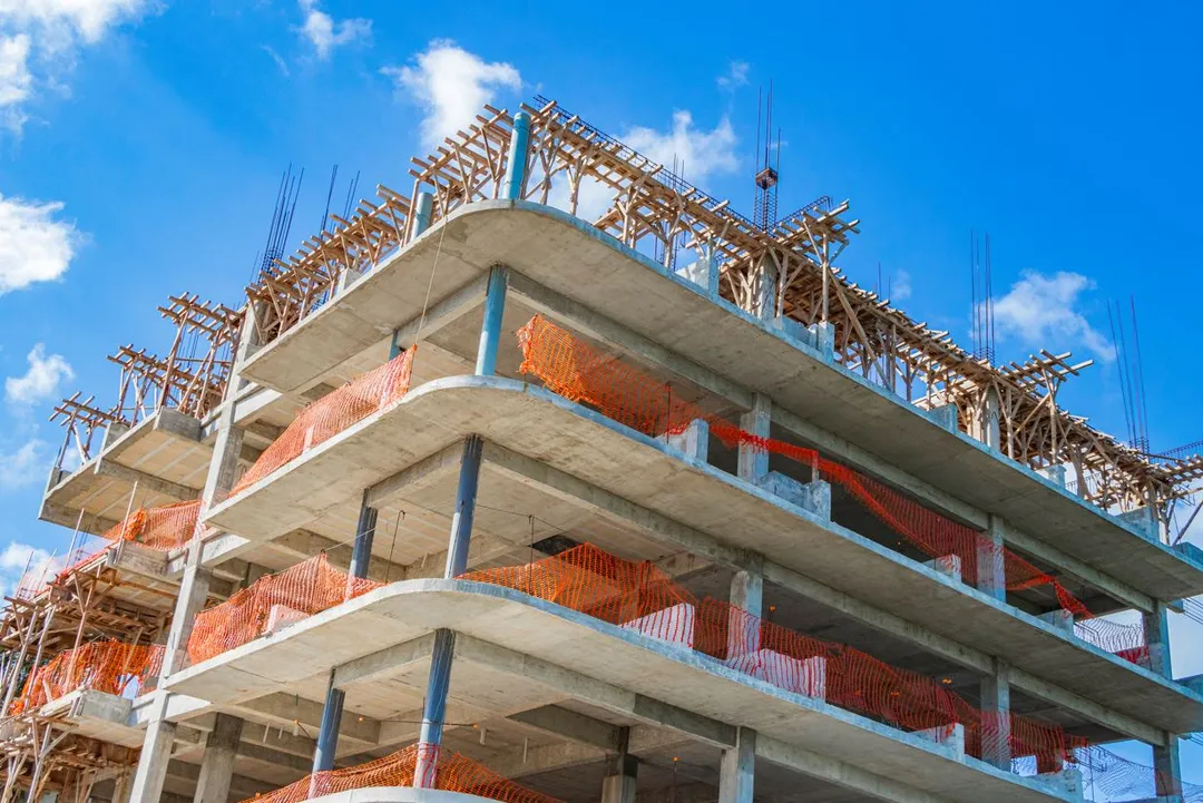 Tulum Targets Fraudulent Construction Permit Ring Multi-story concrete building under construction with wooden framework and red safety netting against a blue sky