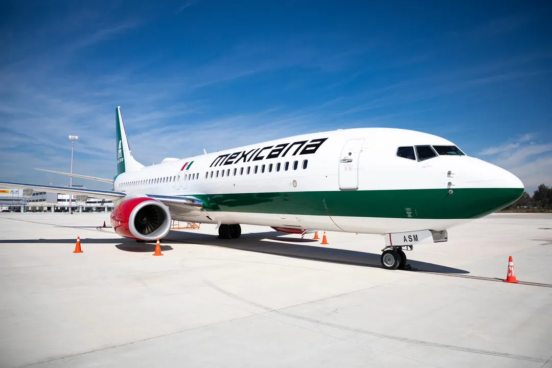 Commercial airliner with white fuselage and green stripe parked on tarmac with ground equipment nearby