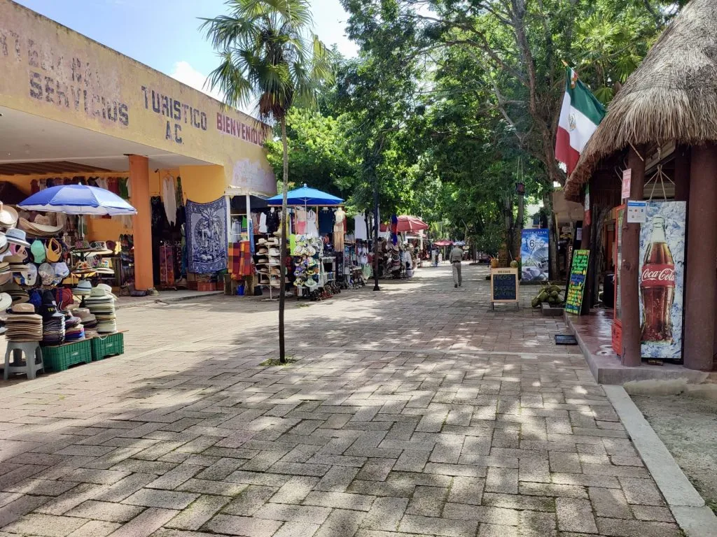 Tulum's Tourism Sector Collapses to 20% of Normal Activity as Workers Abandon Archaeological Zone, Restaurants Close A near-empty market plaza with closed vendor stalls, blue umbrellas, and a Mexican flag flying above shuttered shops