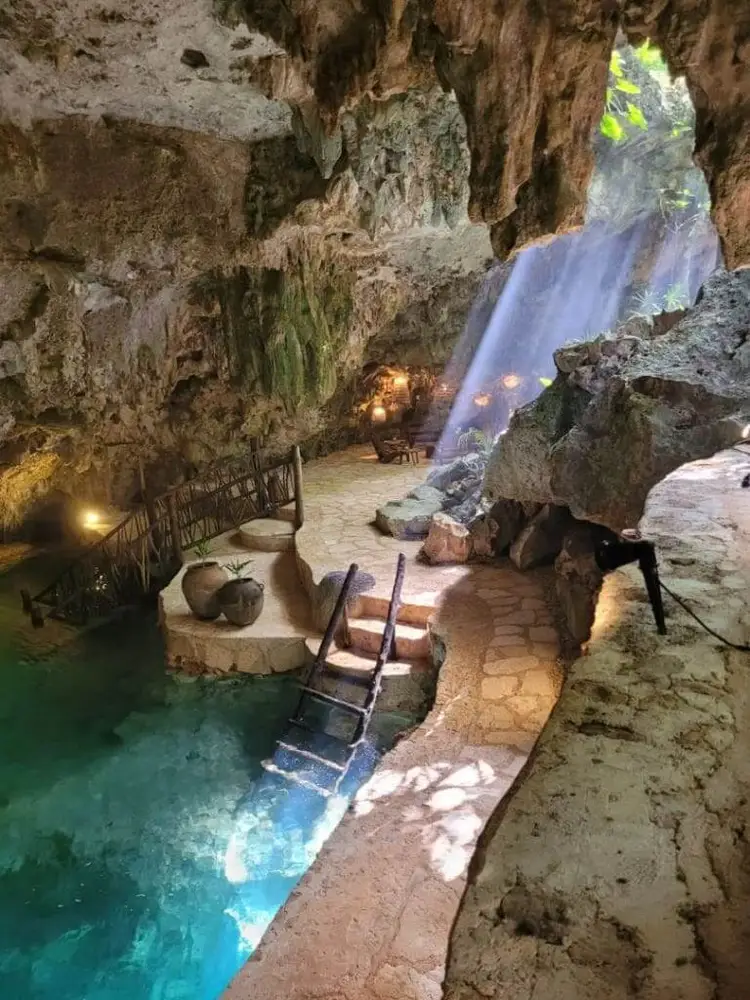 Underground cave chamber with turquoise water, stone walkway, wooden stairs, and a waterfall flowing from an opening above Underground cave chamber with turquoise water, stone walkway, wooden stairs, and a waterfall flowing from an opening above