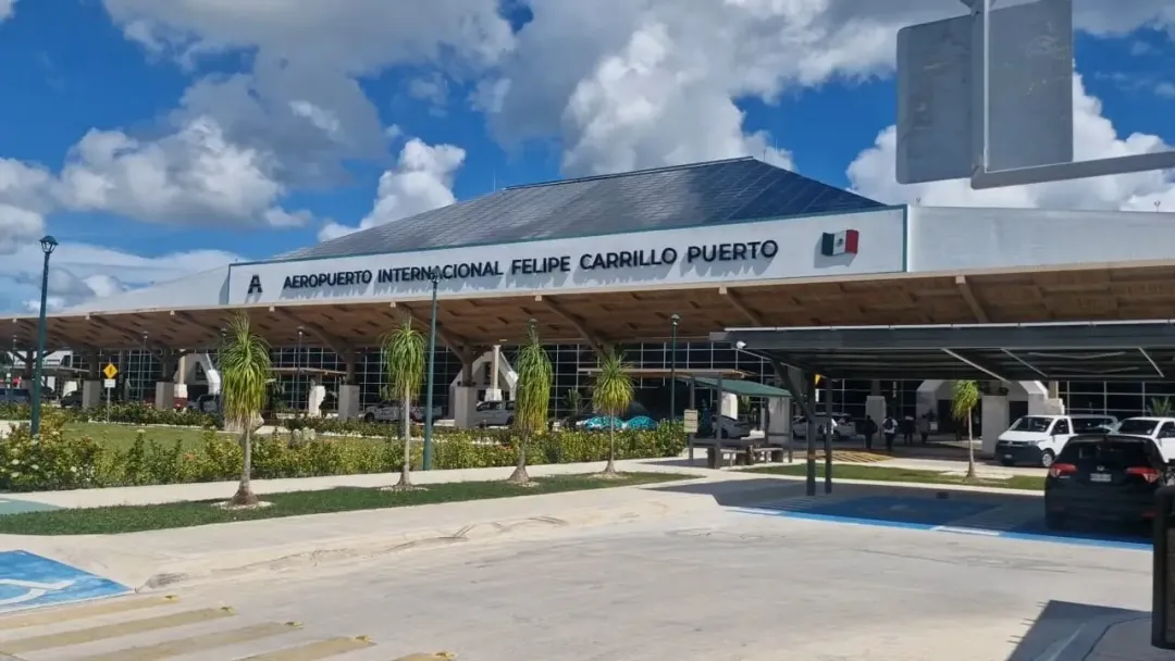 Tulum Airport Loses a Third of International Passengers Airport terminal building with covered entrance area, vehicles parked outside, and landscaping under blue sky with white clouds