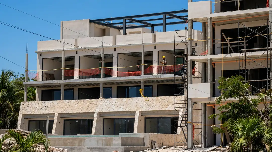 Environmental Groups Call for a Halt to New Tulum Real Estate Development Approvals Multi-story concrete building under construction with metal scaffolding and safety barriers against a clear blue sky