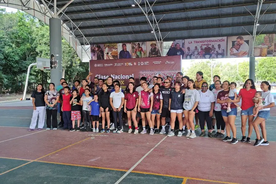 Large group of people standing together on an indoor sports court under a metal roof structure with banners behind them