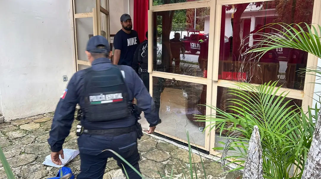 Gunfire Hits Hotel Bacab in Tulum as Attackers Leave a Threat Law enforcement officers investigate outside a building with red-trimmed windows and glass doors, with potted plants nearby