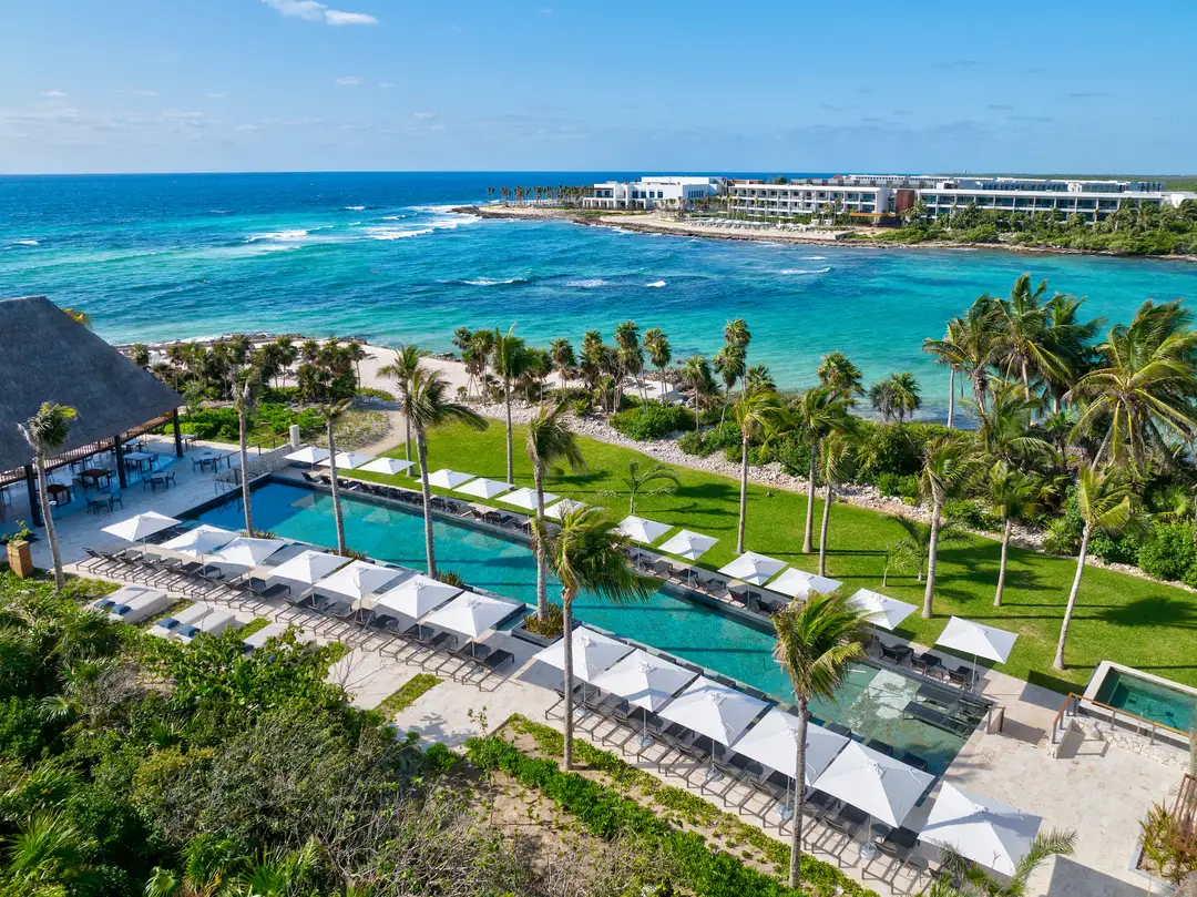 Hilton converts Waldorf Astoria and Conrad Tulum to all inclusive Resort pools and beachfront with white umbrellas overlook turquoise ocean water and sandy beach lined with palm trees
