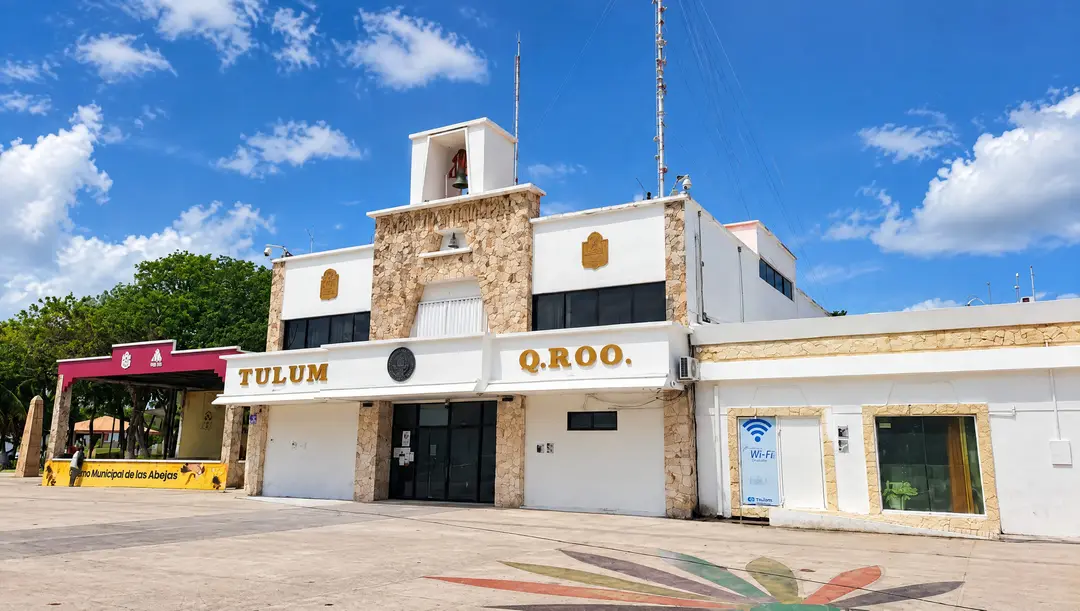 Municipal building with stone and white facade stands in a plaza under clear blue sky with clouds