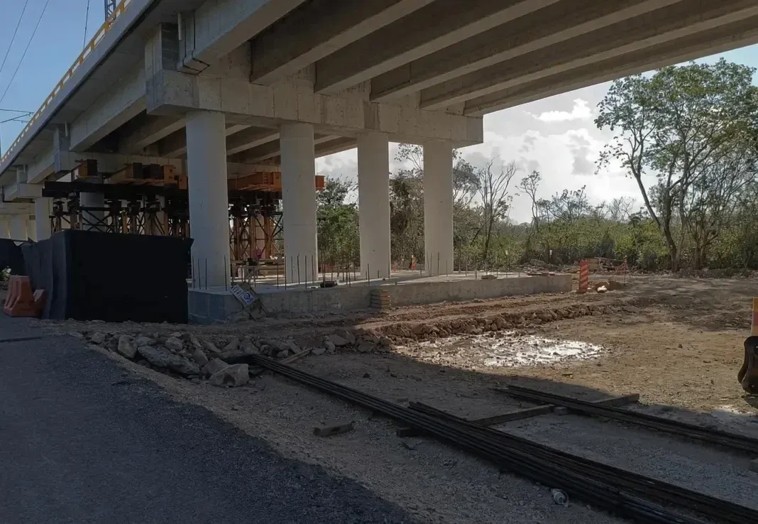 Large concrete bridge under construction spanning over cleared land with trees and construction equipment visible beneath the structure
