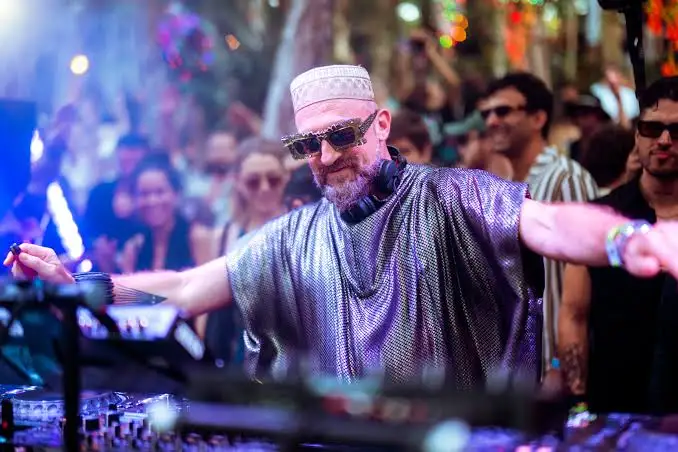 DJ wearing sunglasses and a pink cap performs at a nightclub in front of a crowd