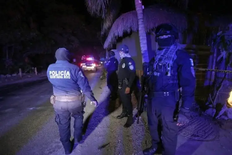 Police officers gather on a nighttime street outside a residential building with police vehicles visible in the background