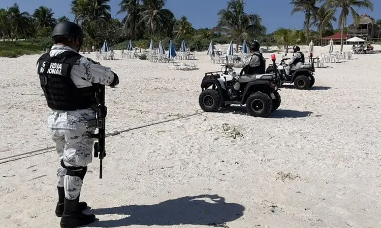 Armed officer stands on beach while patrolling past all-terrain vehicles near umbrellas and palm trees Armed officer stands on beach while patrolling past all-terrain vehicles near umbrellas and palm trees