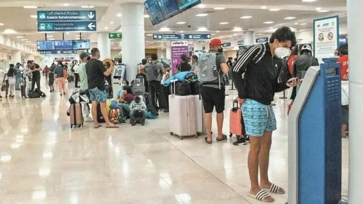 Travelers with luggage queue at check-in counters in an airport terminal