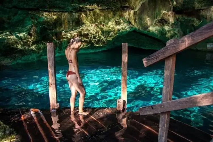 Shirtless man standing on wooden dock above turquoise water surrounded by rocky limestone cliffs and moss-covered cave walls Shirtless man standing on wooden dock above turquoise water surrounded by rocky limestone cliffs and moss-covered cave walls