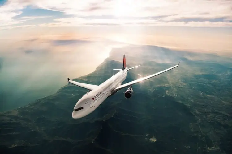 Commercial airliner flying above mountainous terrain with clouds below