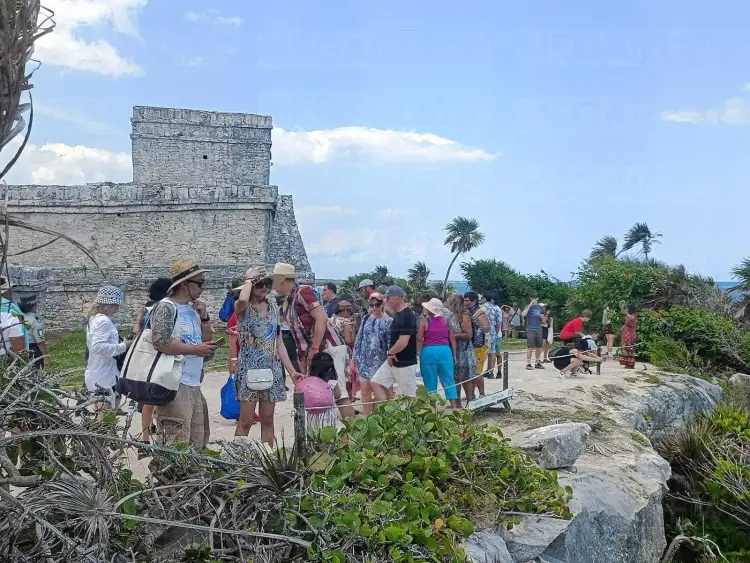 Tourists gather around a stone structure at an archaeological site with palm trees and tropical vegetation visible in the background Tourists gather around a stone structure at an archaeological site with palm trees and tropical vegetation visible in the background