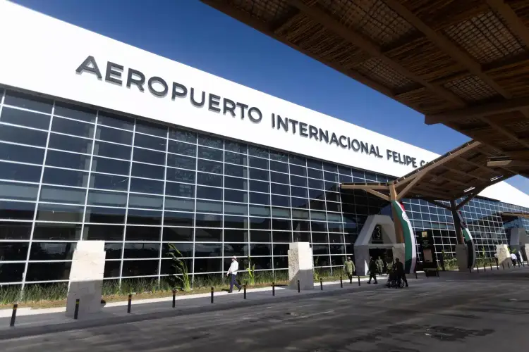 Modern airport terminal building with large glass facade and "Aeropuerto Internacional Felipe Ángeles" signage, with passengers walking near the entrance on a s