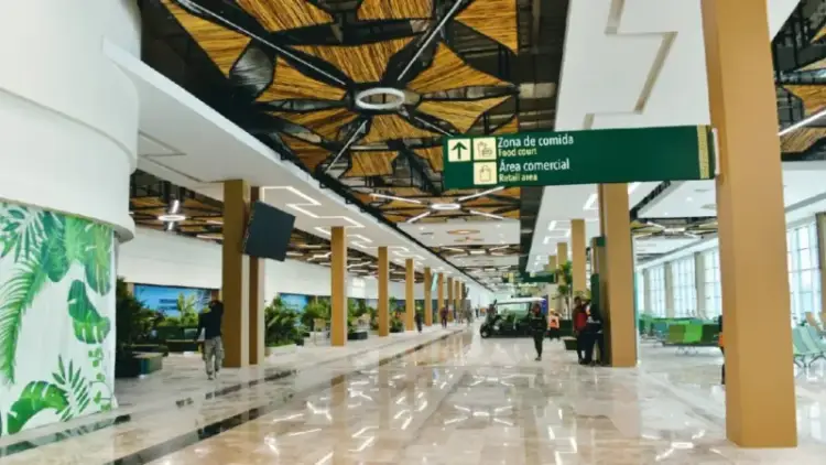 Modern airport terminal corridor with polished floors, yellow support columns, directional signage, and a few travelers walking in the distance