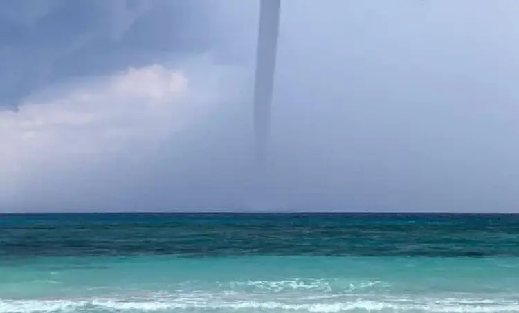 Waterspout forming over turquoise ocean water with waves in the foreground under a cloudy sky Waterspout forming over turquoise ocean water with waves in the foreground under a cloudy sky