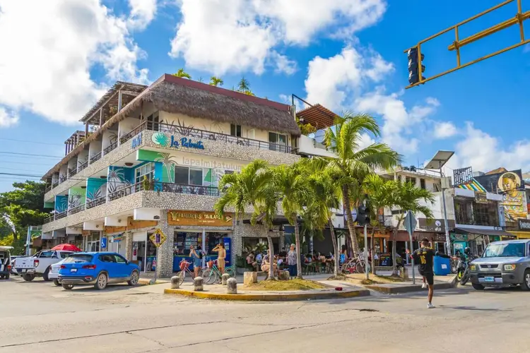 Multi-story beachfront buildings with thatched roofing house shops and restaurants along a street lined with palm trees and parked cars Multi-story beachfront buildings with thatched roofing house shops and restaurants along a street lined with palm trees and parked cars