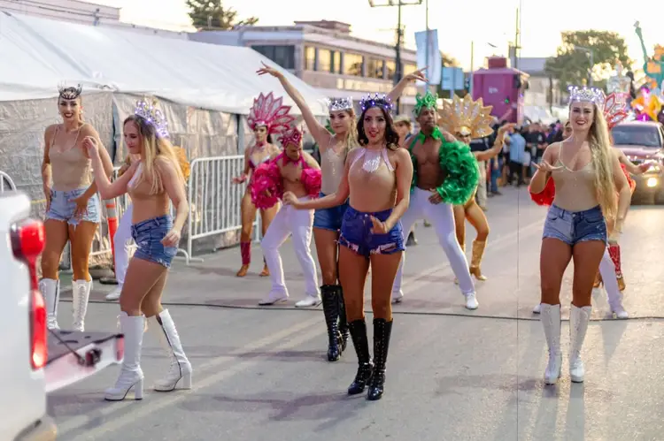 Performers in colorful costumes and headdresses dance down a street during a carnival celebration
