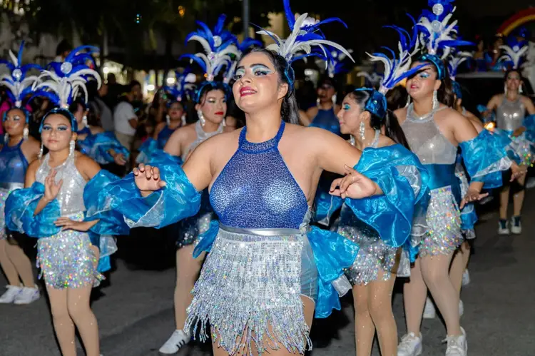 Carnival performers in blue and silver sequined costumes with elaborate feathered headdresses dance in a nighttime street parade