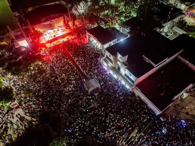 Aerial view of a large crowd gathered in a street at night watching a concert stage with red and white lighting illuminating the venue