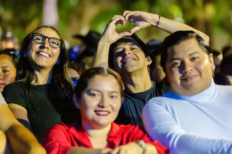 Group of young people smiling and making a heart shape with their hands at a nighttime outdoor gathering
