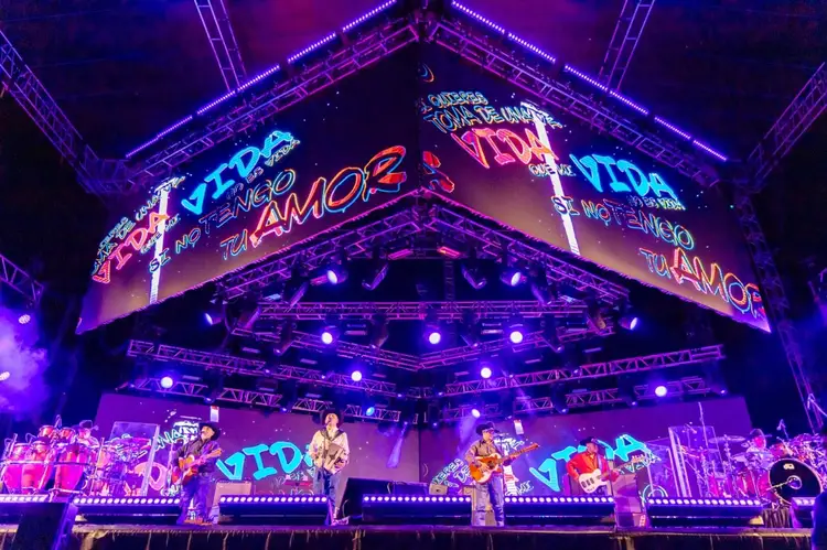 Band performs on illuminated stage with neon signage and purple lighting at an indoor concert venue