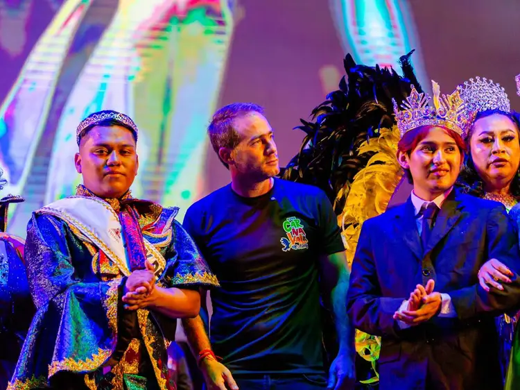 Group of people on stage wearing colorful costumes and crowns under purple and neon lighting