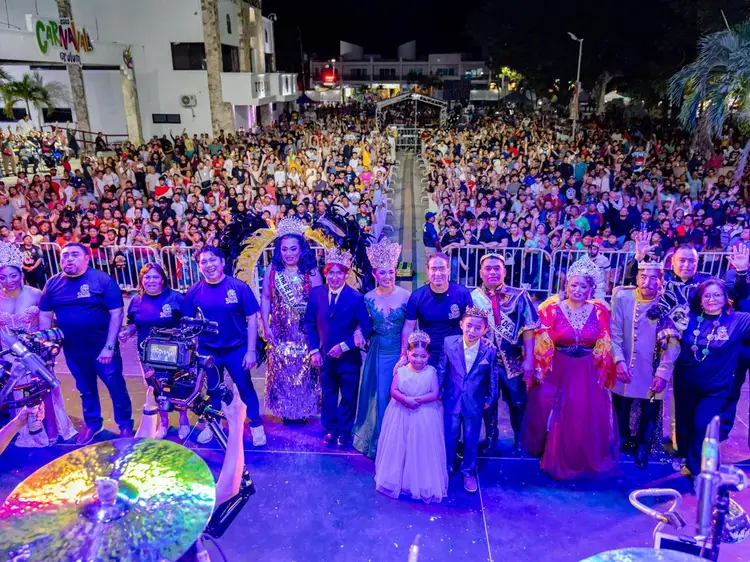 Large crowd gathers at night for a carnival celebration with performers and officials on an illuminated stage