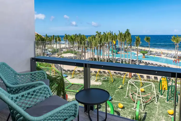 Turquoise wicker chairs and a small table on a balcony overlooking a beachfront resort with palm trees, pool, and ocean Turquoise wicker chairs and a small table on a balcony overlooking a beachfront resort with palm trees, pool, and ocean