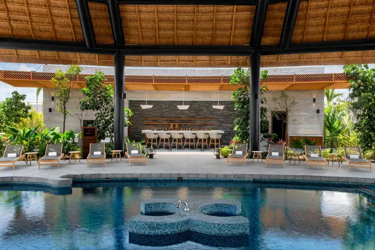 Swimming pool with lounge chairs and a pergola-covered pavilion featuring a bar and seating area overlooking the water Swimming pool with lounge chairs and a pergola-covered pavilion featuring a bar and seating area overlooking the water