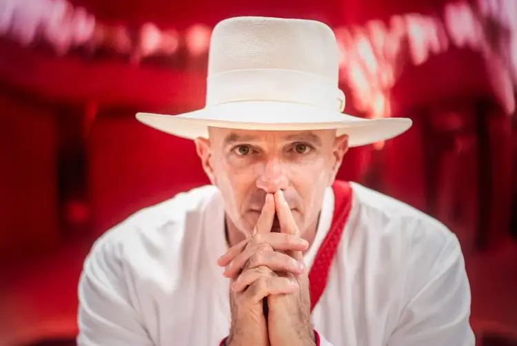Man in white hat and red neckerchief with hands clasped near his face against a red blurred background Man in white hat and red neckerchief with hands clasped near his face against a red blurred background
