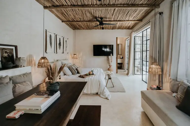 Spacious bedroom with woven ceiling, white walls, a bed with neutral bedding, dark wood furniture, pendant lights, and glass doors leading to an outdoor area