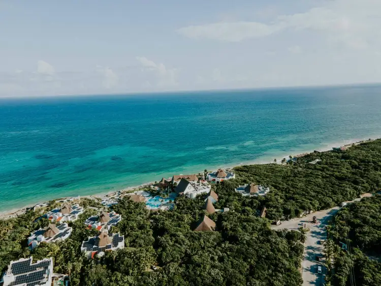 Aerial view of a beachfront resort development nestled among dense jungle vegetation, with turquoise ocean waters and white sand beach visible beyond