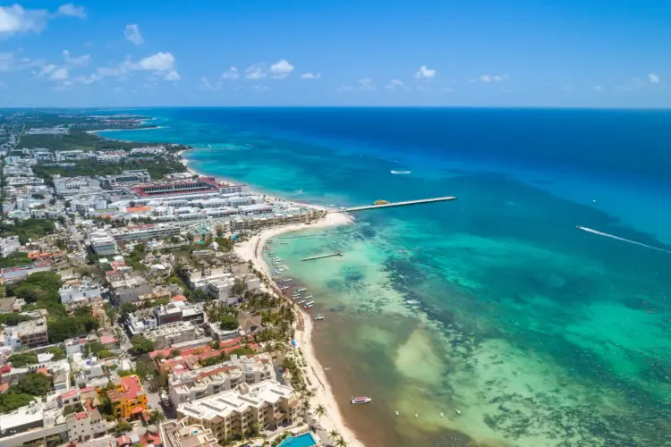 Aerial view of a coastal resort town with beachfront hotels, residential buildings, and turquoise waters with boats offshore