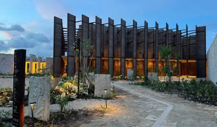 Modern building with dark wooden slat exterior and illuminated amber windows, surrounded by planted gardens and pathways at dusk Modern building with dark wooden slat exterior and illuminated amber windows, surrounded by planted gardens and pathways at dusk