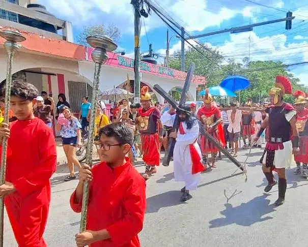 Participants in red clothing carry wooden crosses down a street during a religious procession as spectators line the sidewalks under umbrellas Participants in red clothing carry wooden crosses down a street during a religious procession as spectators line the sidewalks under umbrellas