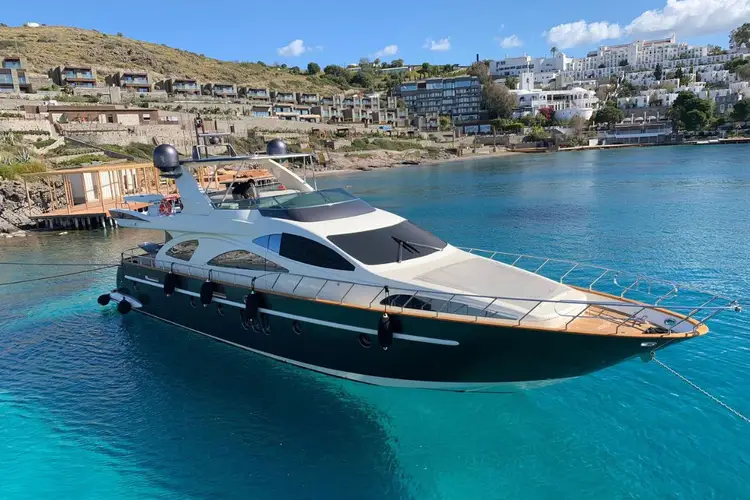 A luxury motor yacht anchored in turquoise water near a hillside coastal town with white buildings