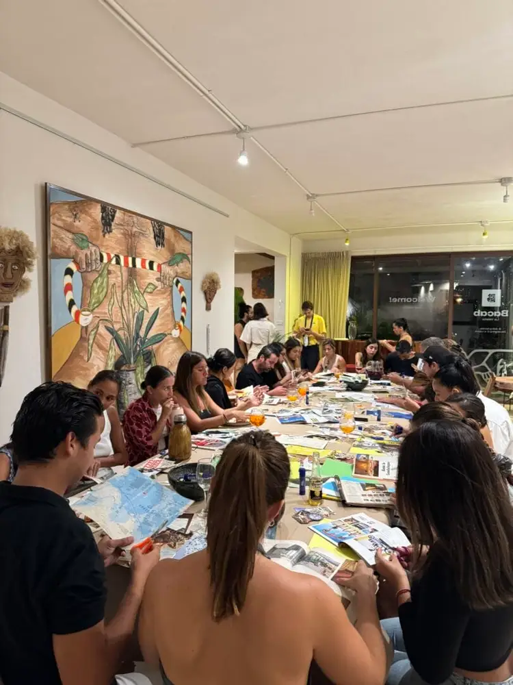 Group of people sitting around a long table with art supplies and magazines at an indoor community event or workshop Group of people sitting around a long table with art supplies and magazines at an indoor community event or workshop
