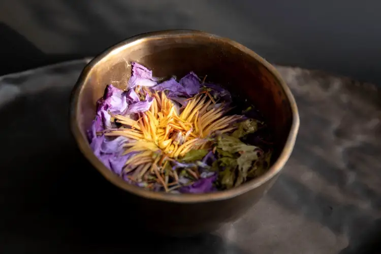 Dried flowers and herbs sit in a small bronze bowl on a dark surface